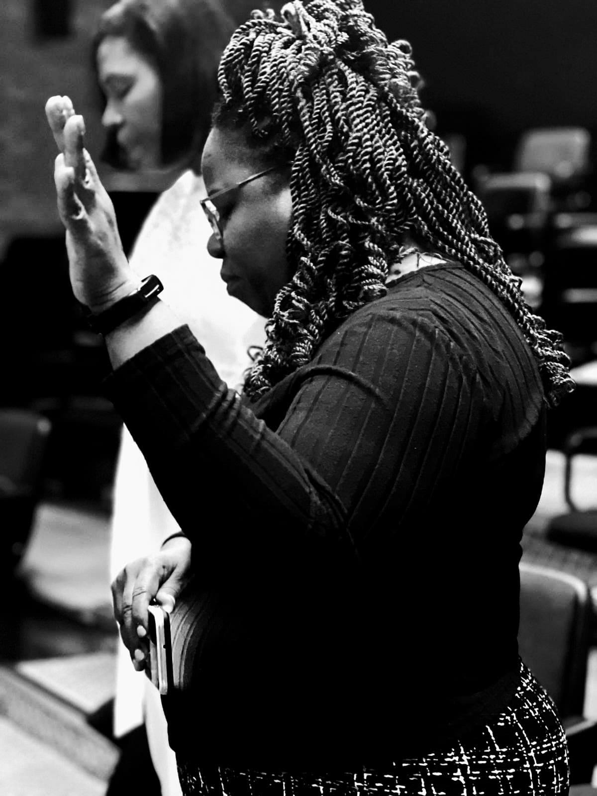 Woman with long braids bows her head and raises a hand in prayerful worship.