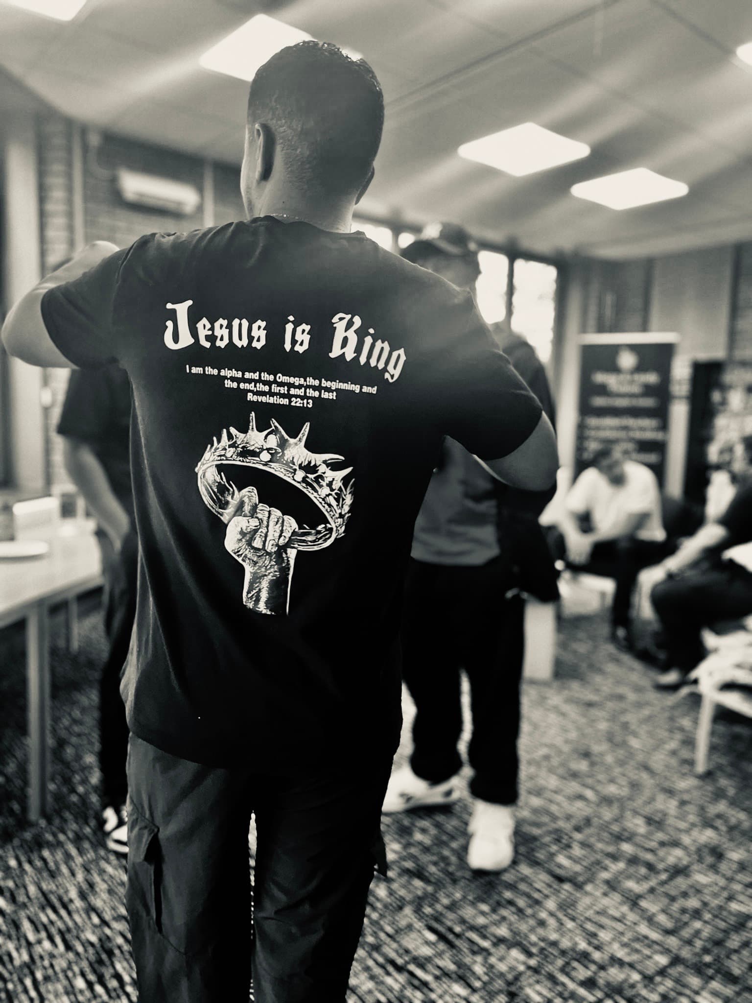 Man's back wearing a black t-shirt with 'Jesus is King' and a crown graphic.