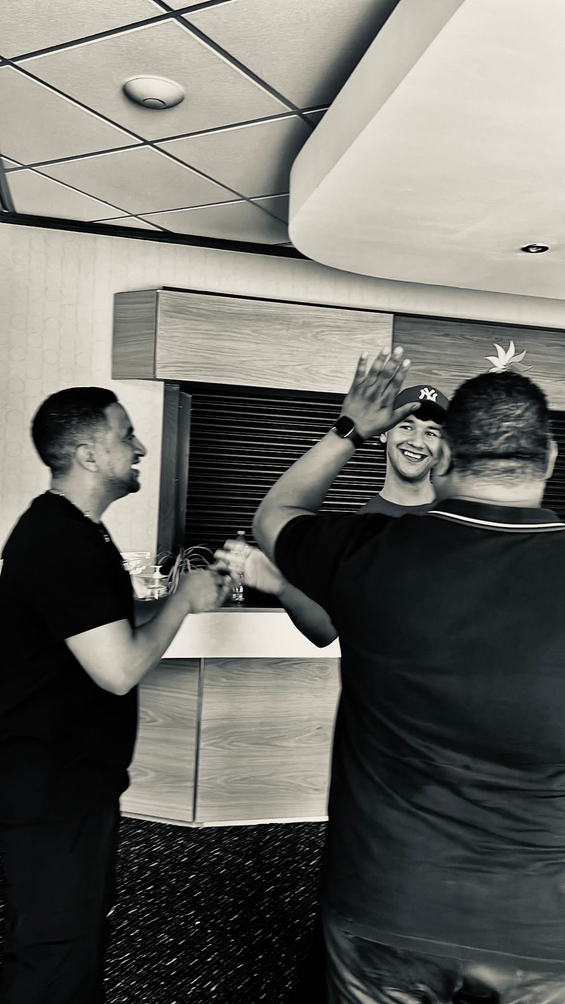 Three men smiling and high-fiving in a black and white photo inside a modern lounge.
