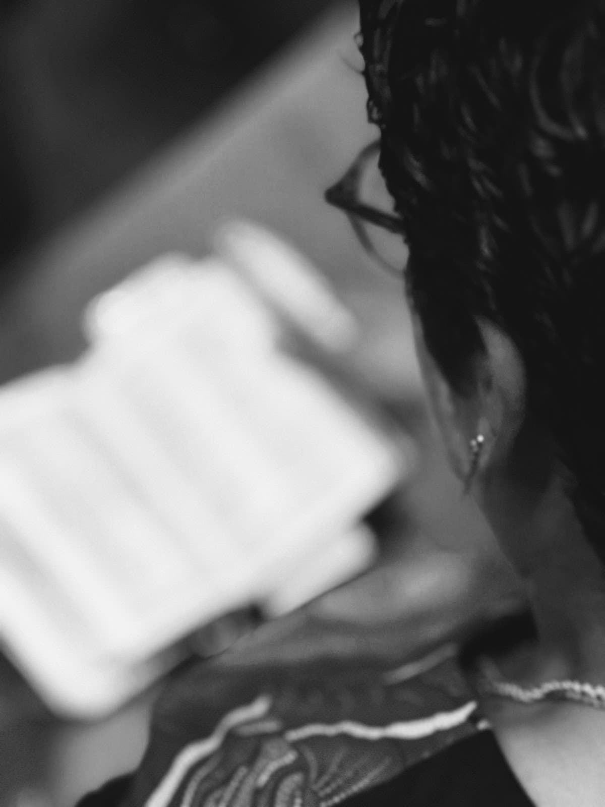 Artistic black and white shot from behind a person with glasses reading a blurred book.