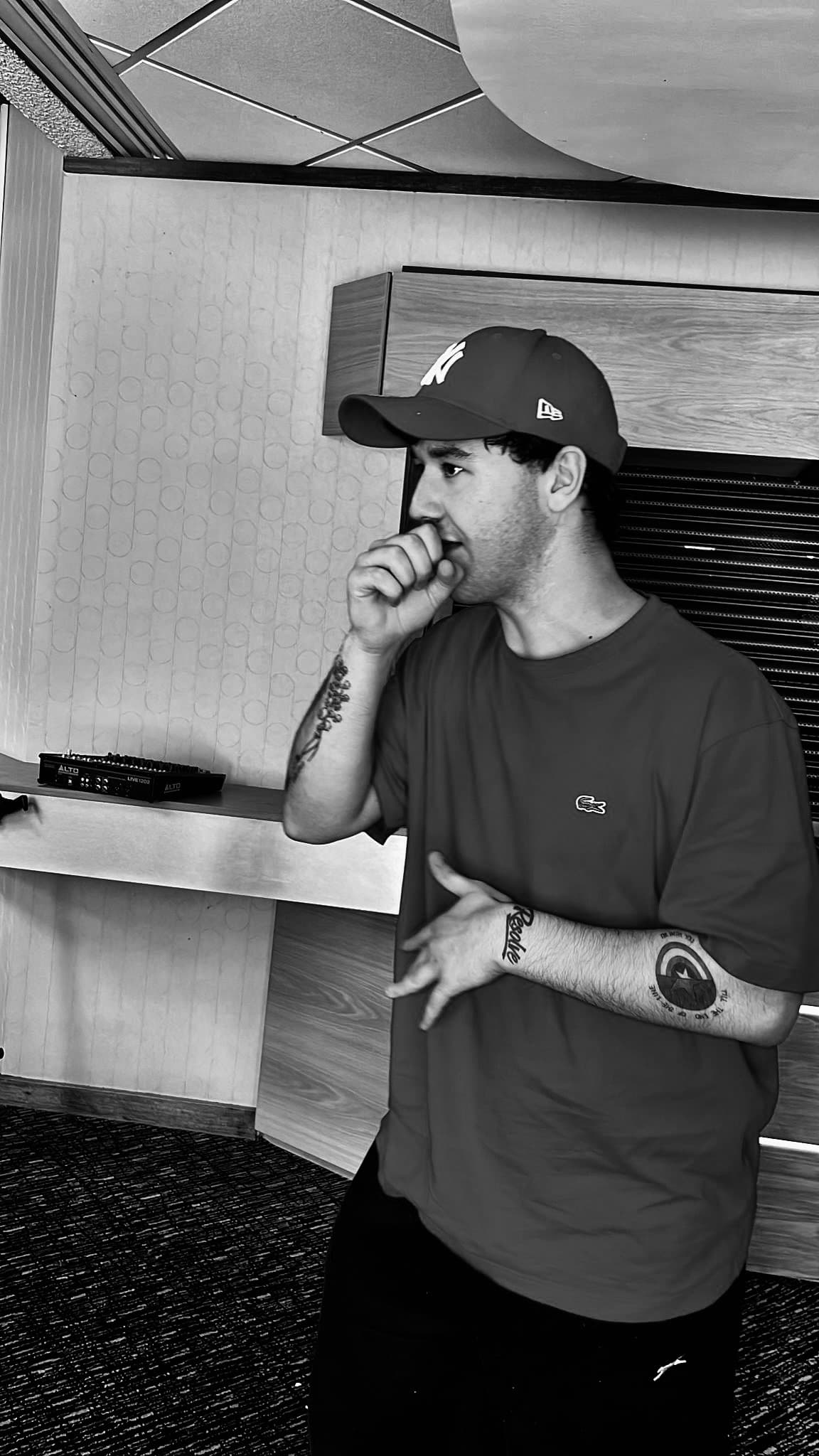 Black and white shot of a tattooed man in a cap gesturing in a studio.