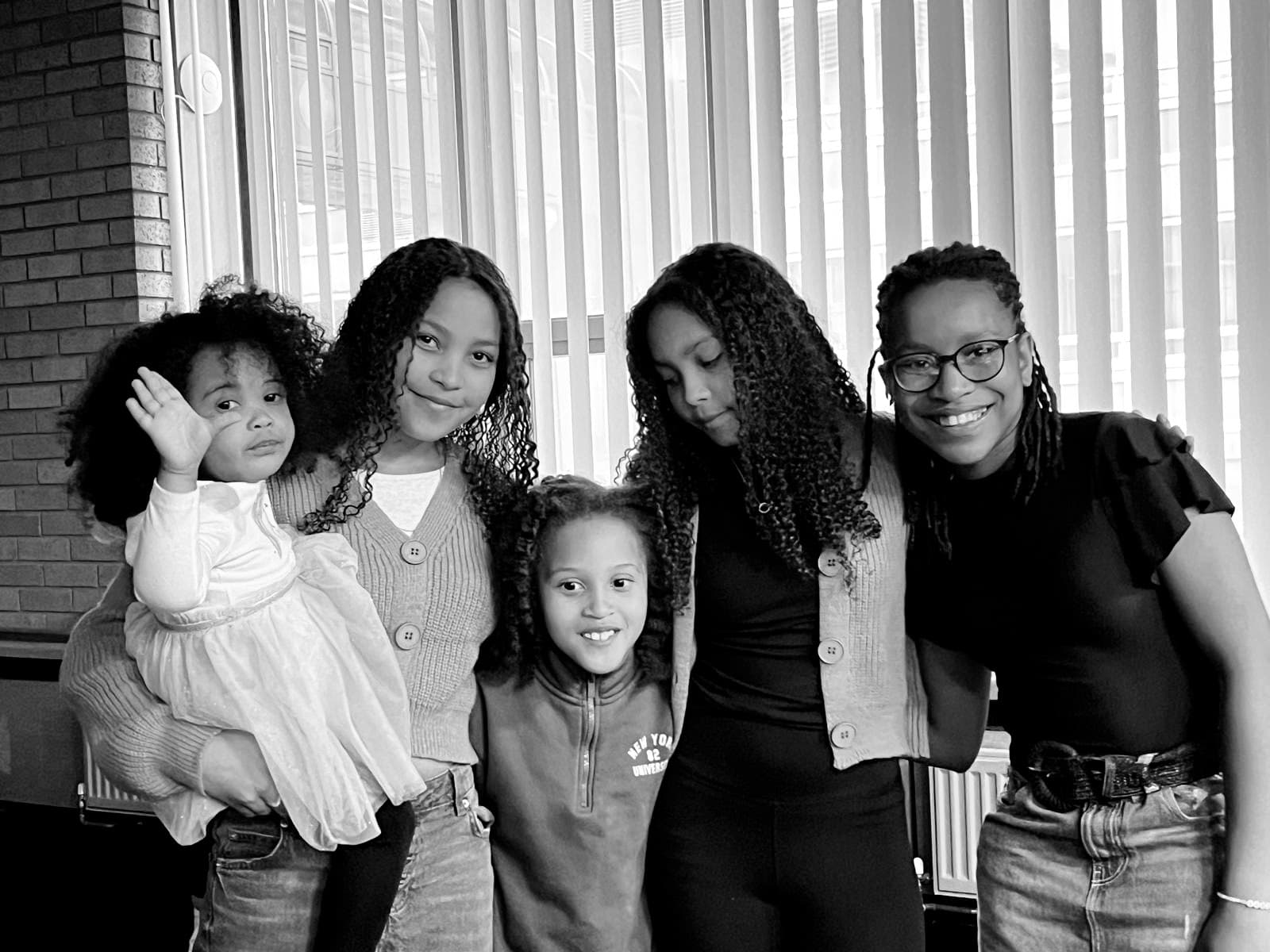 Five Black girls of various ages smile together in a black and white group portrait.